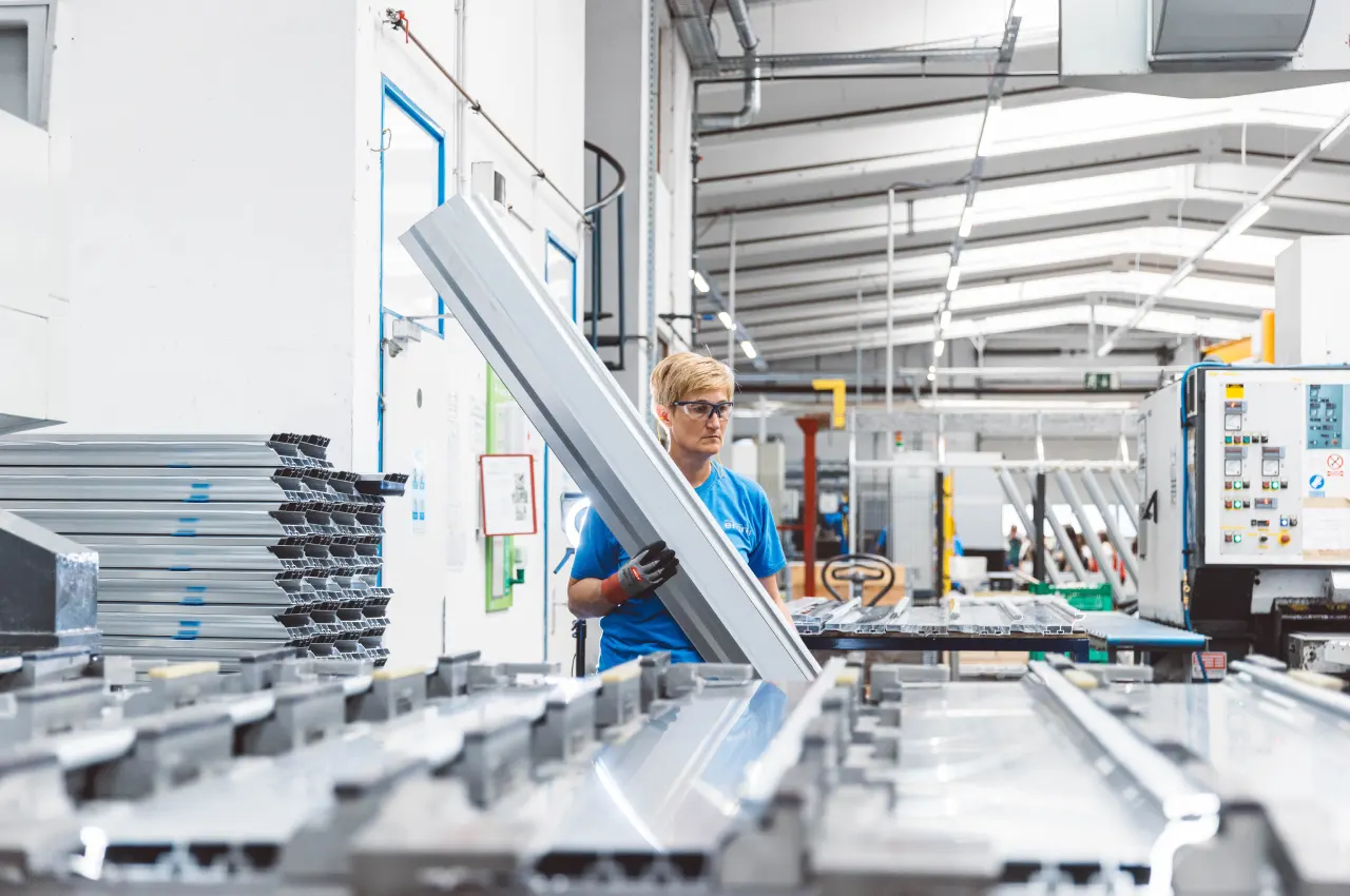 Mitarbeiterin beim Einlegen eines Aluminiumprofils in eine Maschine
